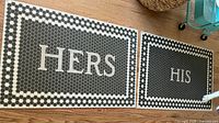 Full view of the "HERS" and "HIS" vinyl bath mats side by side on wooden floor showing hex tile pattern and text