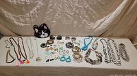 Wide view of entire lot including jewelry spread out on a surface, beaded cat purse, and sunglasses