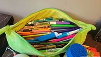 Open green banana-shaped zippered bag filled with assorted colored pencils and markers in various colors.