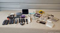 Full lot display including Nintendo 3DS XL, tablet, multiple remotes, cables, earbuds, yellow speaker, and purple USB adapter