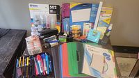 Overall view of office supplies bundle showing Epson 502 ink set, folders, binders, pens, pencils, markers, folders and Post-it notes.