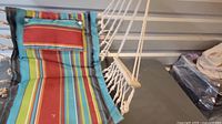 Close-up view of cotton rope hanging chair with colorful striped fabric seating showing macrame ropes, highlighting condition needing rope repair.
