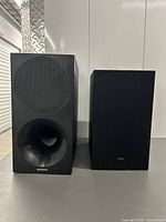 Photo showing two Samsung subwoofers with front-facing grills and bass ports on a tabletop.