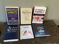 Six self-help and recovery books displayed on a surface against a gray wall, titles visible.