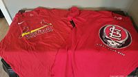 Photo of two red St. Louis Cardinals baseball T-shirts side by side on table.