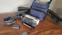 Sony digital camcorder with black battery, charger, AV cables and blue carrying case on wooden surface.