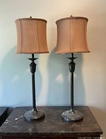 Pair of tall traditional bronze table lamps with beige fabric shades, showing full height and design.