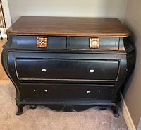 Full front view of vintage wooden chest of drawers with 4 drawers, black painted body and brown wooden top. Shows curved shape and leg design.