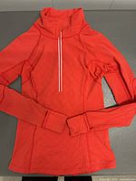 Red women's long-sleeve athletic top with quarter zip collar and subtle diamond pattern on fabric, laid flat.