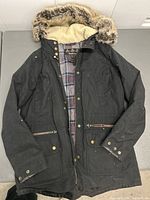 Barbour women's coat black with fur-trimmed hood, plaid lining shown on table