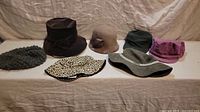 Seven women's bohemian style hats displayed on a white surface with varied textures, colors, and styles.