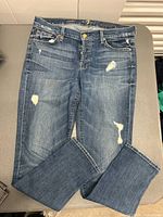Front view of women's blue distressed denim jeans laid flat with visible distress spots and yellow stitching