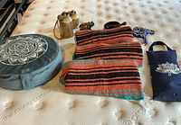 Overview of yoga accessories showing a round meditating cushion with mandala print, three folded striped yoga blankets, fabric pouch, metal bells, brass elephant figurine, and a sound bowl with striker.
