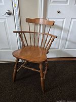 Full view of antique wooden armchair showing its curved backrest, spindles, armrests, and turned legs.