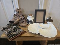 Photo showing all assorted decorative accent items on wooden bench including plush koala, ceramic jar, photo frame, metal flask, ceramic shell dishes, and fabric pot holders.