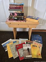 Books and magazines stacked on and around a small wooden bench, showing a range of war-themed titles in various sizes and conditions.