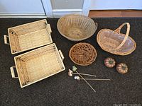 Five wicker baskets of various sizes and shapes, two decorative pumpkins, and three plant decor sticks arranged on a black carpet.