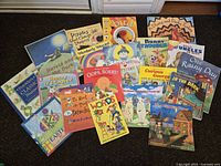 Photo showing a spread of 20 assorted children's books arranged on a dark textile surface.