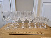 Full view of the set of 8 tall water goblets and 6 smaller sherry glasses arranged on wooden surface with a ruler in front for scale.