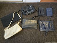 Overview of six assorted purses including various types and styles, mostly black with one cream purse.