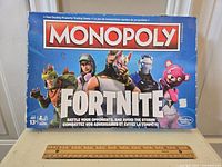 Front view of Fortnite Monopoly board game box showing characters and branding, with ruler for size reference.