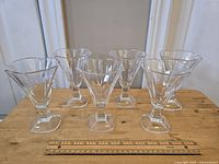 Set of six vintage French crystal glasses arranged on a wooden surface, showing the scalloped V-shaped bowls with square bases and cut feet.