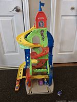 Front view of the colorful Little People Sit 'n Stand Skyway playset with spiral slides and ramps, several small vehicles positioned at base and on ramps.