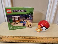 Photo showing the sealed LEGO Minecraft 21251 set box with a ruler for scale, alongside the Pokémon Charmander figure and Poké Ball toy