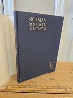 Blue cloth hardcover book titled 'Norman Rockwell Illustrator' with gold embossed text on the front cover.