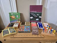 Photo of assorted playing cards, Cribbage game book, golf tees in wooden holder, and boxed game pieces all laid out on a wooden table.