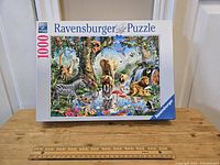 Box of Ravensburger 1000-piece puzzle with jungle animal scene shown, sitting on a wooden surface with ruler for scale.