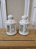 Front view of the pair of white metal candle lanterns with glass sides and star cutouts on top.