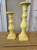 Two buttercream yellow taper candle holders on wood surface against a beige wall; one taller, one shorter
