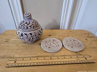 Photo showing carved stoneware vessel and two coasters on wooden surface with ruler for scale.