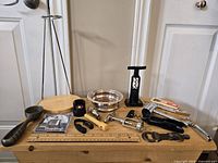 Wide shot of assorted barware items arranged on wooden surface including decanter stand, wine coaster bowl, corkscrews, bottle openers, wine stopper, aerator, and stirring spoon.