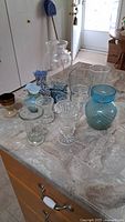 Front view of 12 assorted decorative glassware pieces including vases and bowls on kitchen counter