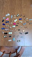 Photo showing 49 pairs of assorted vintage clip-on earrings laid out on a wooden table, displaying the variety in shape, size, color, and design.