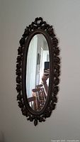 Front view of small oval decorative mirror showing detailed rose pattern metal frame in brown with tarnish.