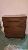 Front view of brown mid-century modern wood dresser showing 4 drawers with minor scratches and curved drawer fronts on the top two drawers.