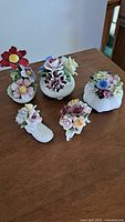 Photo showcasing five porcelain flower bouquet sculptures in various colors and bases on a wooden surface.