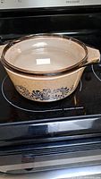 Beige Pyrex casserole dish with blue pattern and glass lid shown on stove