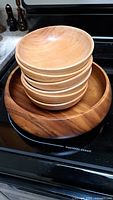 Top view of 6 small wooden bowls stacked inside 1 large darker wooden salad bowl on a stove top, showing the smooth natural wood finish and grain.