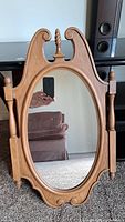 Photo of an oval wall mirror with a carved wooden frame showing traditional design elements including turned posts and decorative scrollwork.