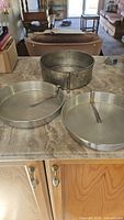 Photo showing all three vintage metal pie pans on a countertop in a home kitchen setting. Two pans are placed inside a larger pan.