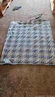 Full view of the electric heated fleece blanket laid flat on carpet, showing plaid pattern and cord attached.