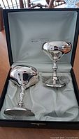 Two polished silverplate goblets inside a lined presentation box with satin-like light green lining.