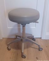 Front view of gray round padded medical stool with five wheels and lever for height adjustment.