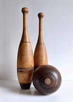 Full view of two antique hardwood exercise clubs with black bands and a wooden lawn bowling ball with brass center disc.