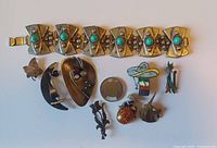 The full set of silver-tone artisan jewelry, highlighting the bracelet with turquoise-colored accents and multiple pins/brooches with various designs including animals, abstract shapes, and amber stones.