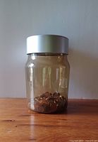 Front view of the clear plastic coin jar mostly filled with pennies, showing the jar shape and content.